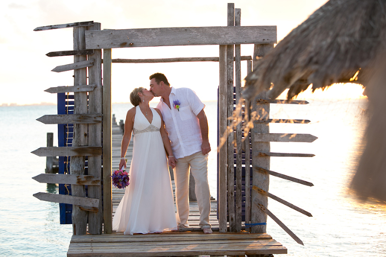 Bride and groom kissing on pier at sunset