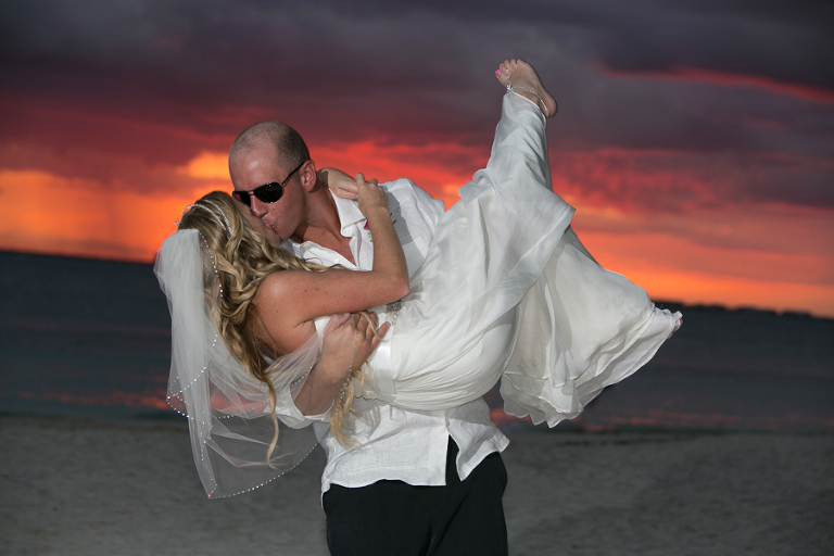 Groom dipping bride at sunset on beach